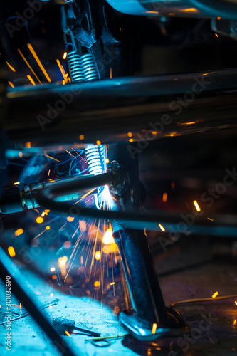 Worker welding a motorcycle metal part in gloves. Freeze motion sparks , close-up.