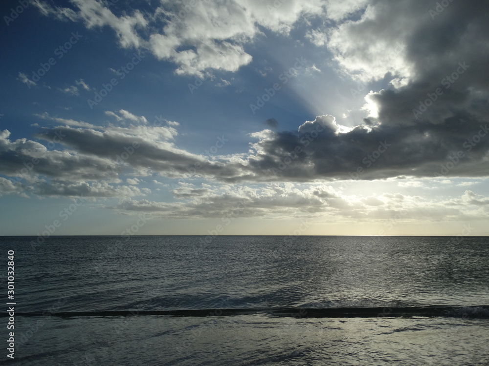 dramatic sun and clouds overcalm ocean water in florida