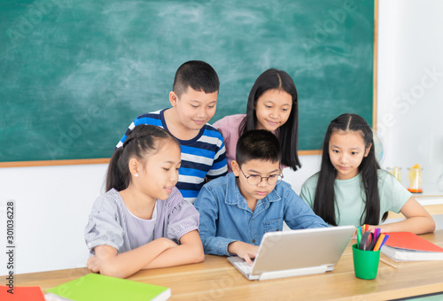 asian children group study in classroom, students feeling happy in education  time, they do work and do project with laptop together on blackboard background, education technology, elementary school