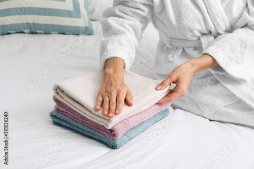 Beautiful young woman stacking clean towels on bed