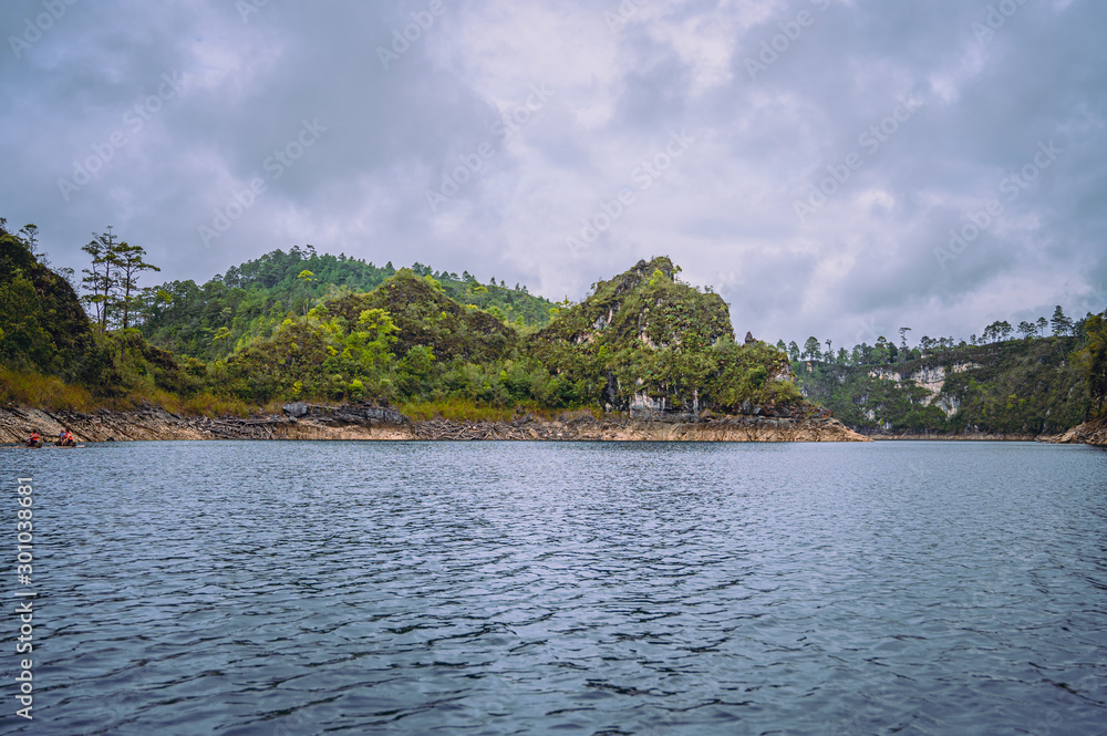Beautiful landscape of a blue lake, in the background wooded mountains in cloudy sky day