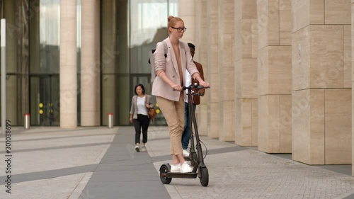 Wide shot of young Caucasian ginger woman and African man on electric kick scooters meeting in city center and starting chat