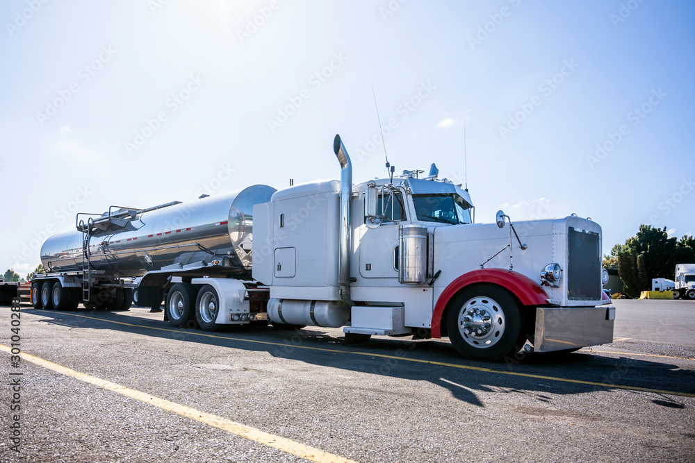 White classic big rig semi truck with tank semi trailer for transporting liquid cargo standing on truck stop parking lot