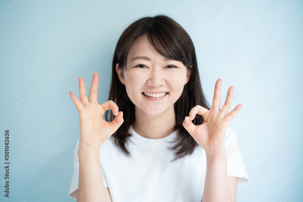 Young woman shoing OK gesture against light blue background Young woman shoing OK gesture against light blue background