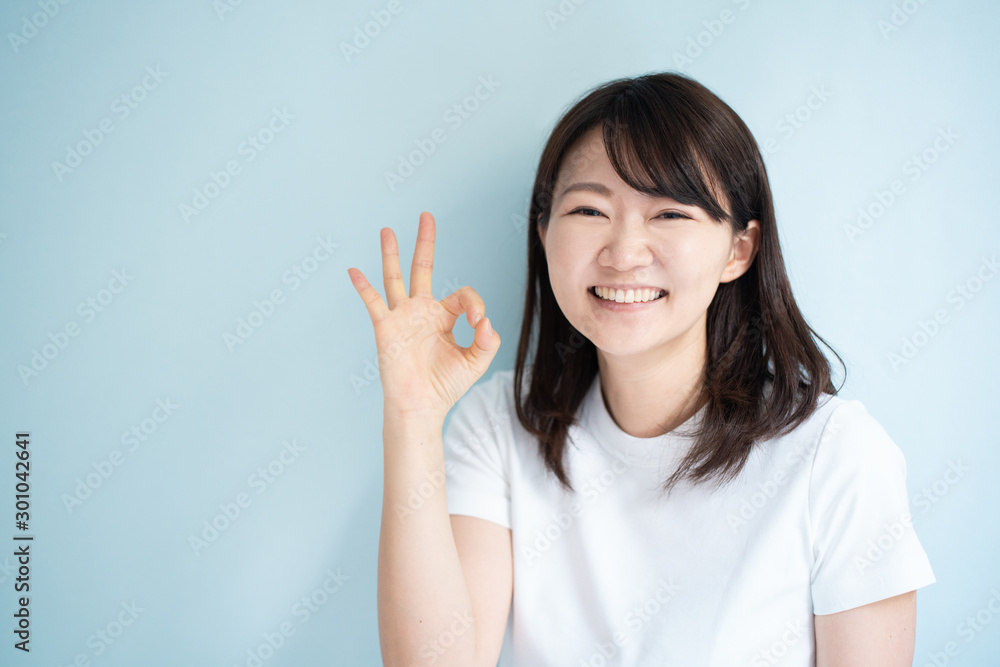 Young woman shoing OK gesture against light blue background Young woman shoing OK gesture against light blue background
