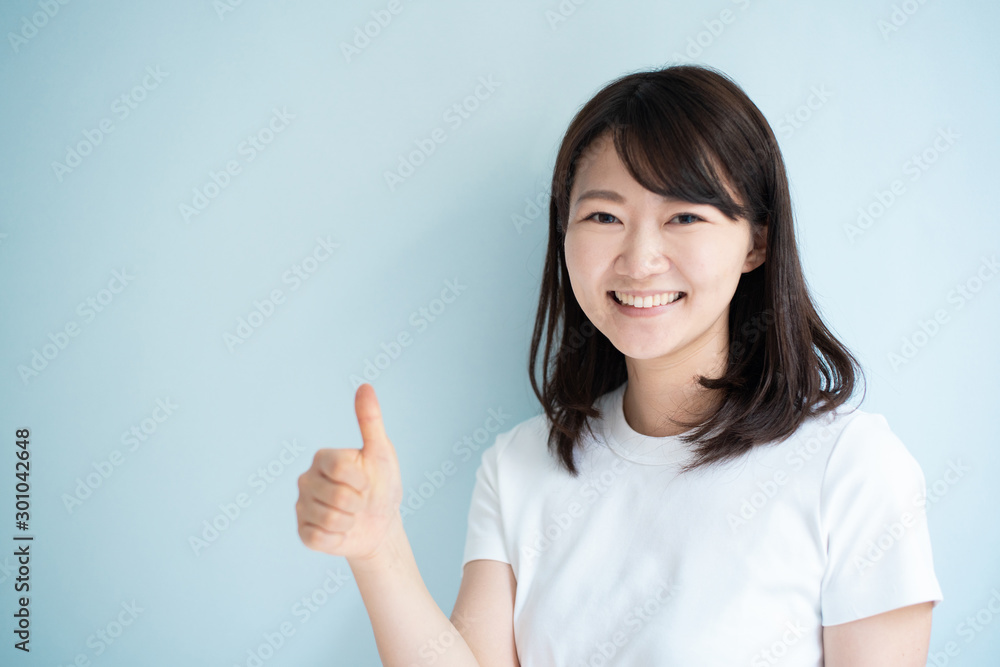 Young woman showing thumb up gesture against light blue background Young woman showing thumb up gesture against light blue background