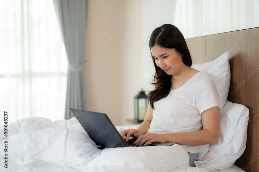 Portrait of beautiful Asian woman relax using laptop in bedroom. Smile happy asian girl online shopping at home Education e-commerce freelance technology connected asia people concept Portrait of beautiful Asian woman relax using laptop in bedroom. Smile happy asian girl online shopping at home Education e-commerce freelance technology connected asia people concept