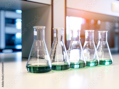 The Erlenmeyer or Conical flasks on bench laboratory, with range of green solvent forming reaction between boric acid and ammonia solution analysis concentration in wastewater sample. Selective focus. photo