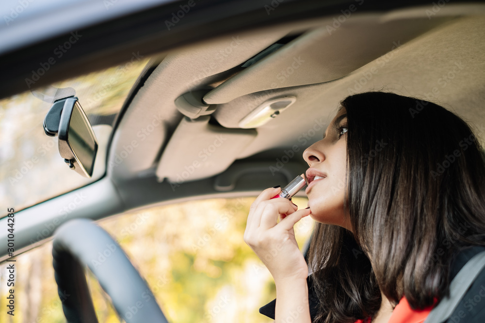 Woman applying lipstick while looking at car mirror Woman applying lipstick while looking at car mirror