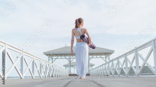 Young women wearing white yoga clothing are preparing to practice meditation on the beach near the sea. On the pier on the Maldives Amazing yoga landscape and enjoying sea views, health care