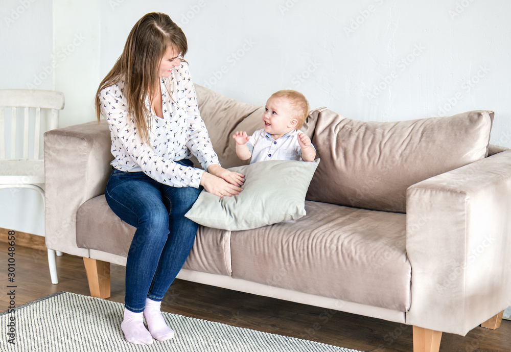 Mom and a little blond boy sit on a cream couch and play a game. Horizontal photography