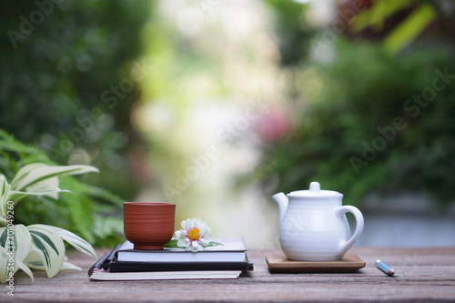 White teapot and vintage cup with flower and notebooks on wooden table