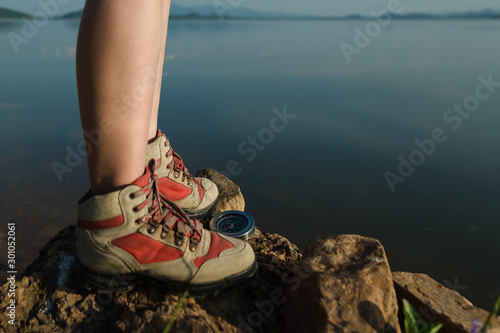 Top view: Hiking shoes with a compass on a rock by the lake in the summer after sunrise. Summer Travel Trekking Concept