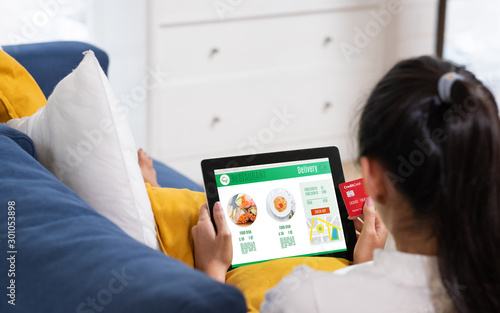 Asian woman order food online with credit card on tablet sitting on sofa at home.digital lifestyle with technology,