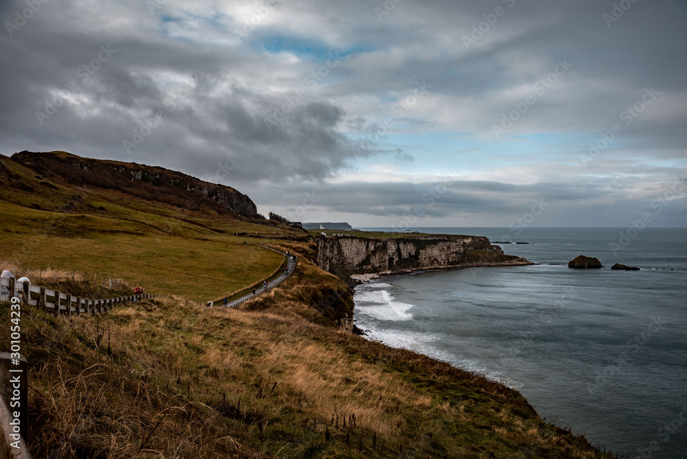 People walking along the coastal pathway during a rainy, cold and cloudy day on the cliffs near Ballintoy in Northern Ireland.