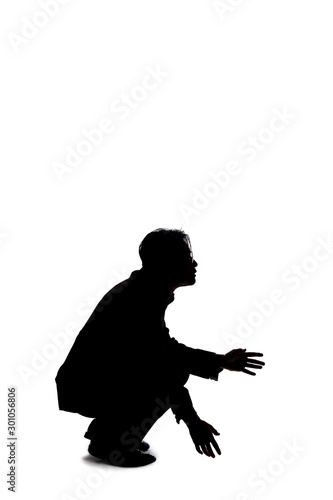 Silhouette of a backlit model posing as a businessman on a white background.  He is crouched on the ground like a detective looking or searching for something on the floor