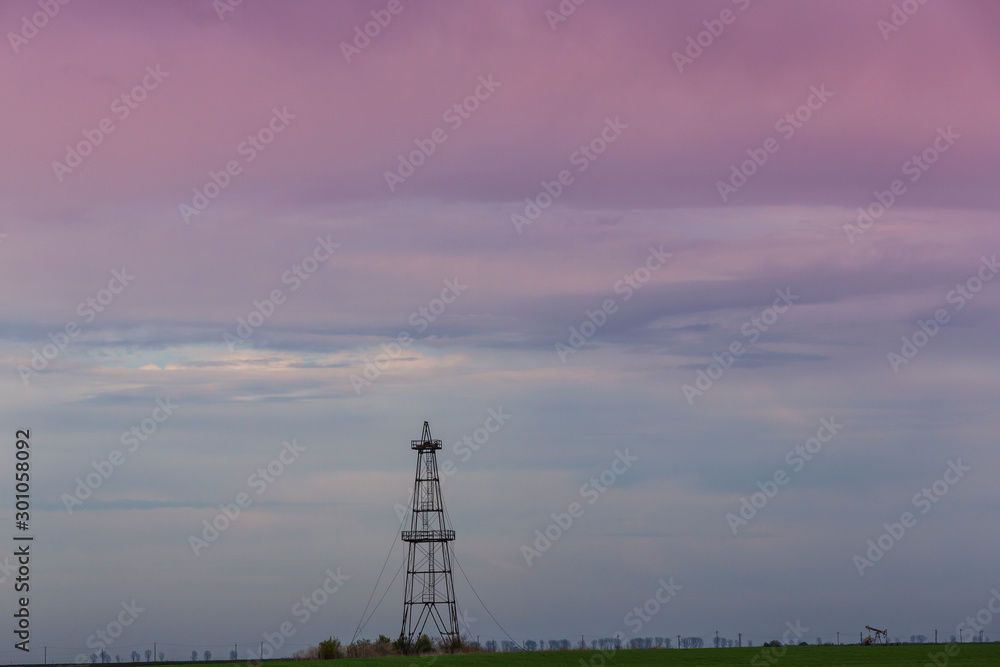 Abandoned oil rig in a field in Eastern Europe,. profiled on background with sunset storm clouds