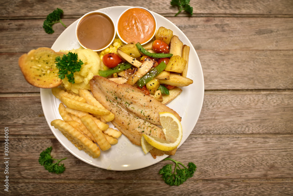 Fish dish - fried fish fillet with fried potatoes and vegetables on wooden rustic background. Top view Fish dish - fried fish fillet with fried potatoes and vegetables on wooden rustic background. Top view