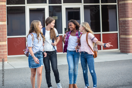 Candid photo of a group of teenage girls socializing, laughing and talking together at school. A multi-ethnic group of real junior high aged students walking outside a school building photo