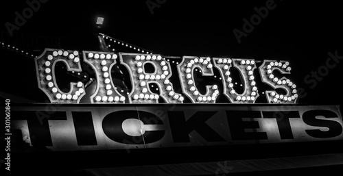 Spooky old dimly lit circus sign with light bulbs in the dark over a ticket stand in black and white. Typical view of an entrance to a circus. Concept of madness and scary.