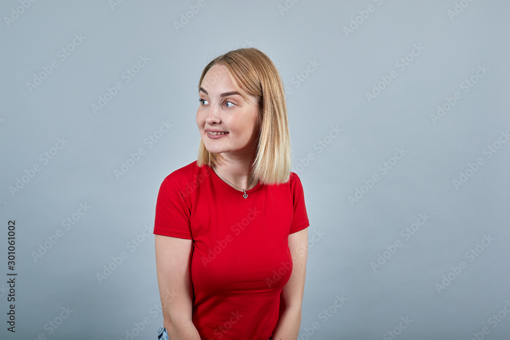 Pretty smiling cheery young woman in knitted red shirt looking aside isolated on grey wall background, studio portrait. People sincere emotions, lifestyle concept. Pretty smiling cheery young woman in knitted red shirt looking aside isolated on grey wall background, studio portrait. People sincere emotions, lifestyle concept.