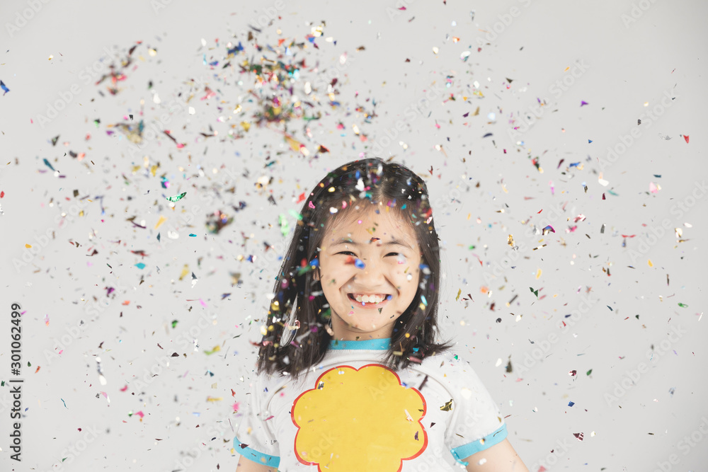 Asian girl having fun with colorful confetti on gray background. Asian girl having fun with colorful confetti on gray background.