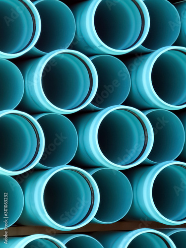 PVC plastic pipes stacked at the construction site ready to be laid as a sewer line.  Interesting contrast between highlights and shadows produces patterns of straight lines and circular end view.