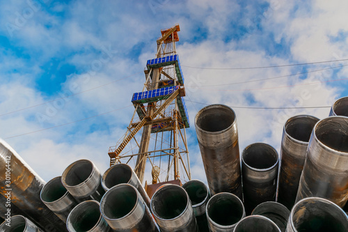 In the foreground pipes for drilling oil and gas wells. In the background is a drilling rig. Blue sky with clouds.