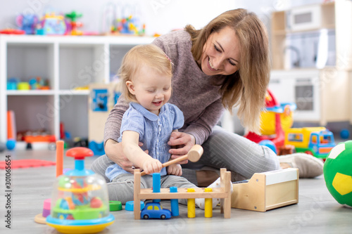 Cheerful baby playing with toys with happy mother in nursery room