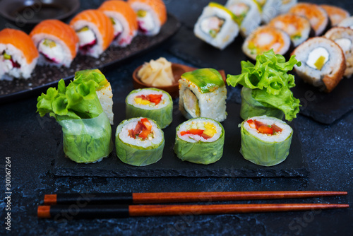Set of vegetarian sushi rolls with lettuce leaves, vegetables and Chinese chopsticks on a black background. Traditional Japanese food.
