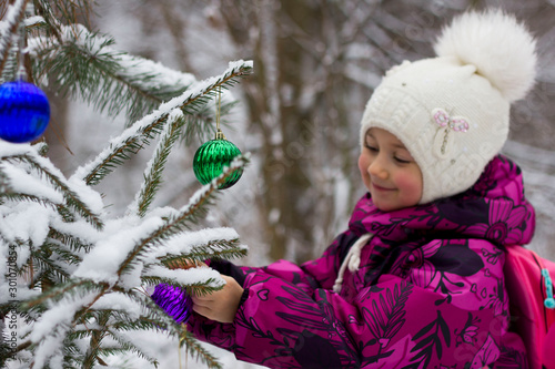 little girl dresses up a Christmas tree in winter in a snowy forest photo