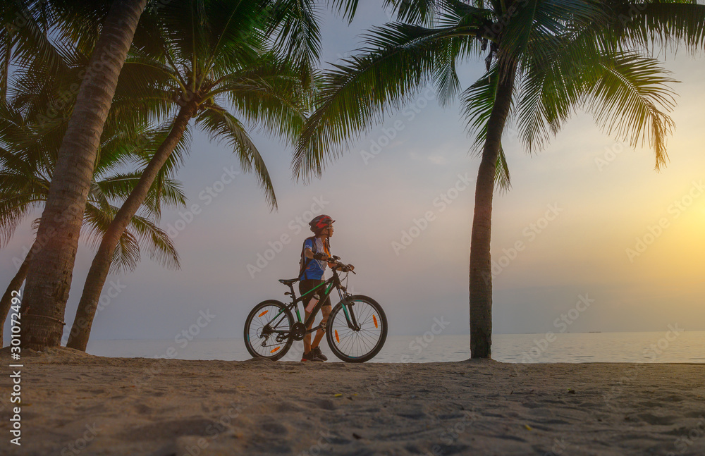 Fototapeta premium woman riding bicycle along the sea beach under coconut trees at sunset, relaxation at the end of the day