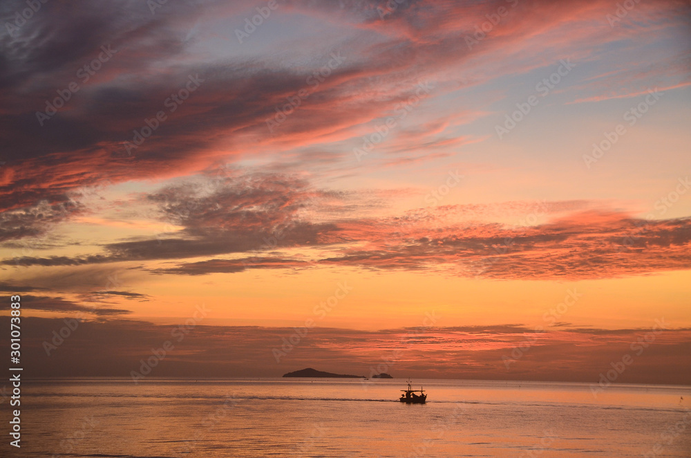  Tropical vibrant coastal pink red sunrise waterscape with a blue sky over ocean water. Huay Yang, Thailand.