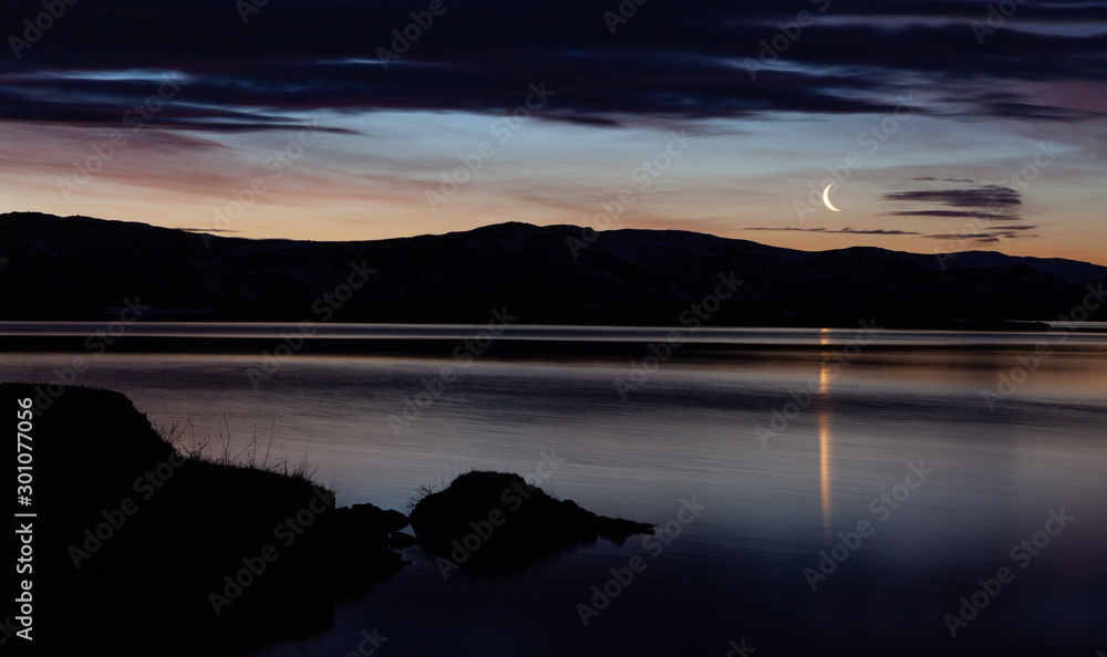 Thingvellir National Park Iceland: sunrise view of lake with reflections of the sky (moon and clouds)