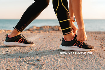 Concept of new year and new success. Sport. A woman in black workout leggings ties her shoelaces on her sneakers. Text NEW YEAR NEW YOU