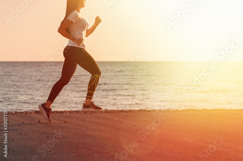 Sports and Jogging along the sea. A young brunette woman runs along the path along the seashore. In the background, the sea and sky in the setting sun. Close up and copy space