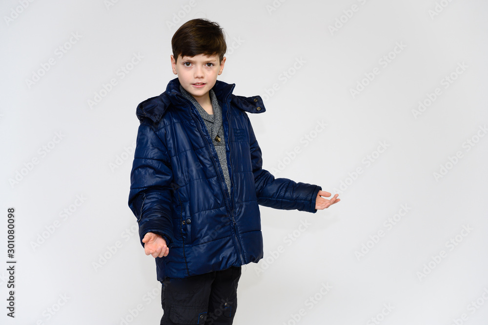 The concept of winter and warm clothes for a teenager boy. Portrait of a baby boy on a white background in a winter jacket and pants. Stands in front of the camera in different poses with emotions. The concept of winter and warm clothes for a teenager boy. Portrait of a baby boy on a white background in a winter jacket and pants. Stands in front of the camera in different poses with emotions.