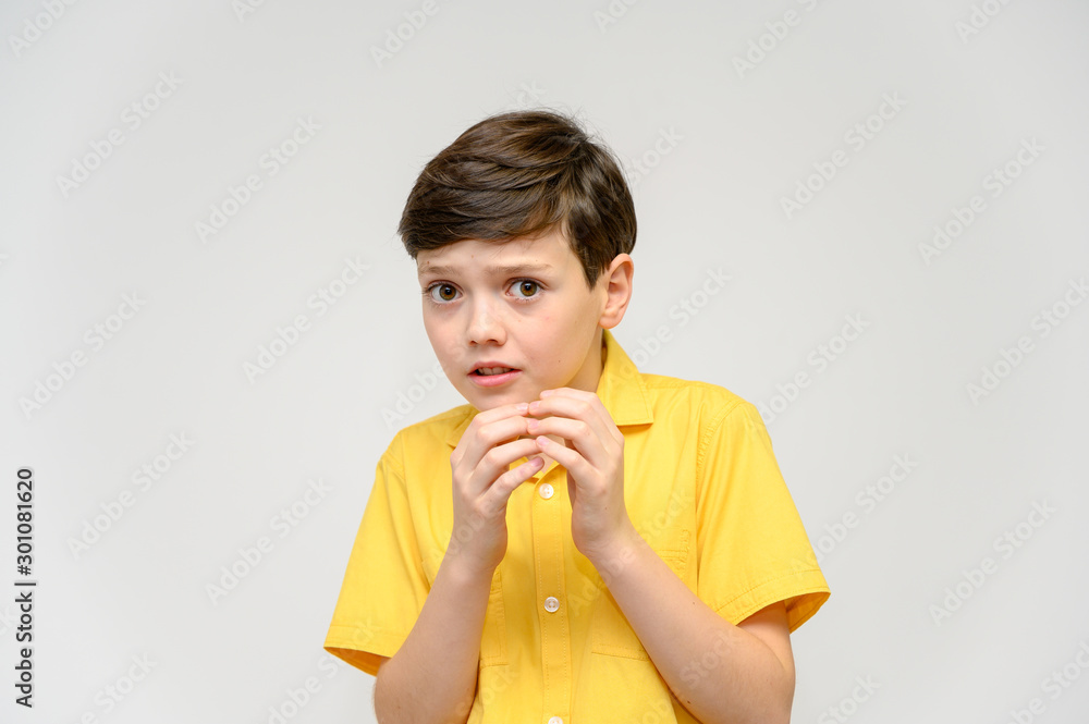 Concept boy teenager shows imitates the behavior of heroes from different movies. Portrait of a child on a white background in a yellow shirt. Standing in front of the camera in poses with emotions. Concept boy teenager shows imitates the behavior of heroes from different movies. Portrait of a child on a white background in a yellow shirt. Standing in front of the camera in poses with emotions.