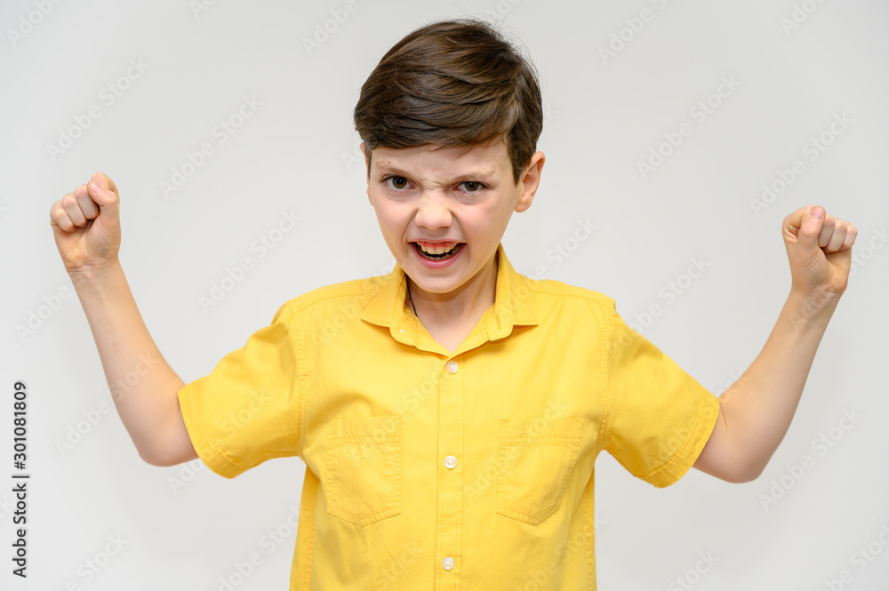 Concept boy teenager shows imitates the behavior of heroes from different movies. Portrait of a child on a white background in a yellow shirt. Standing in front of the camera in poses with emotions. Concept boy teenager shows imitates the behavior of heroes from different movies. Portrait of a child on a white background in a yellow shirt. Standing in front of the camera in poses with emotions.