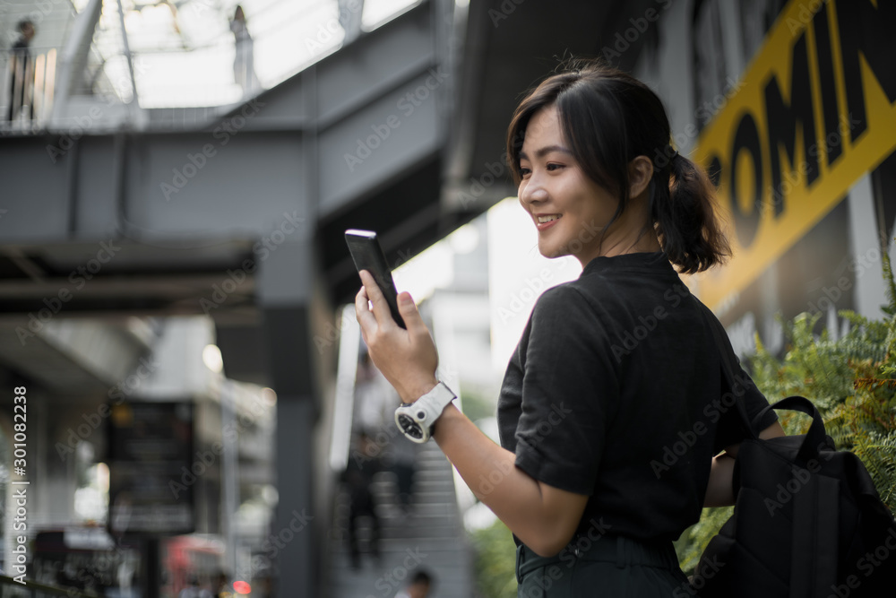Happy asian woman looking at her phone in the city - obrazy, fototapety, plakaty 