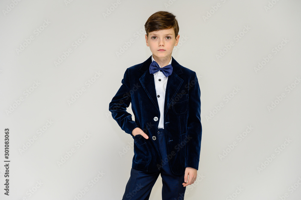 Concept boy teenager shows imitates entertainer behavior on stage. Portrait of a child on a white background in a dark blue concert suit. Standing in front of the camera in poses with emotions. Concept boy teenager shows imitates entertainer behavior on stage. Portrait of a child on a white background in a dark blue concert suit. Standing in front of the camera in poses with emotions.