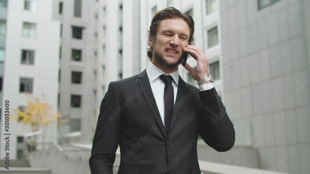 A businessman in business clothes is talking on a cell phone in the courtyard of an office center. The man is angry and argues with the interlocutor. A businessman in business clothes is talking on a cell phone in the courtyard of an office center. The man is angry and argues with the interlocutor.