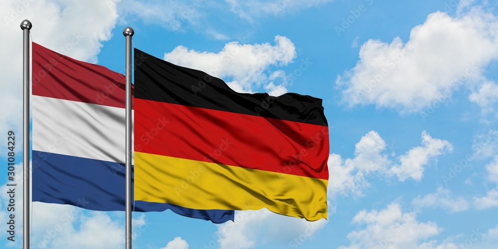 Netherlands and Germany flag waving in the wind against white cloudy blue sky together. Diplomacy concept, international relations. Netherlands and Germany flag waving in the wind against white cloudy blue sky together. Diplomacy concept, international relations.