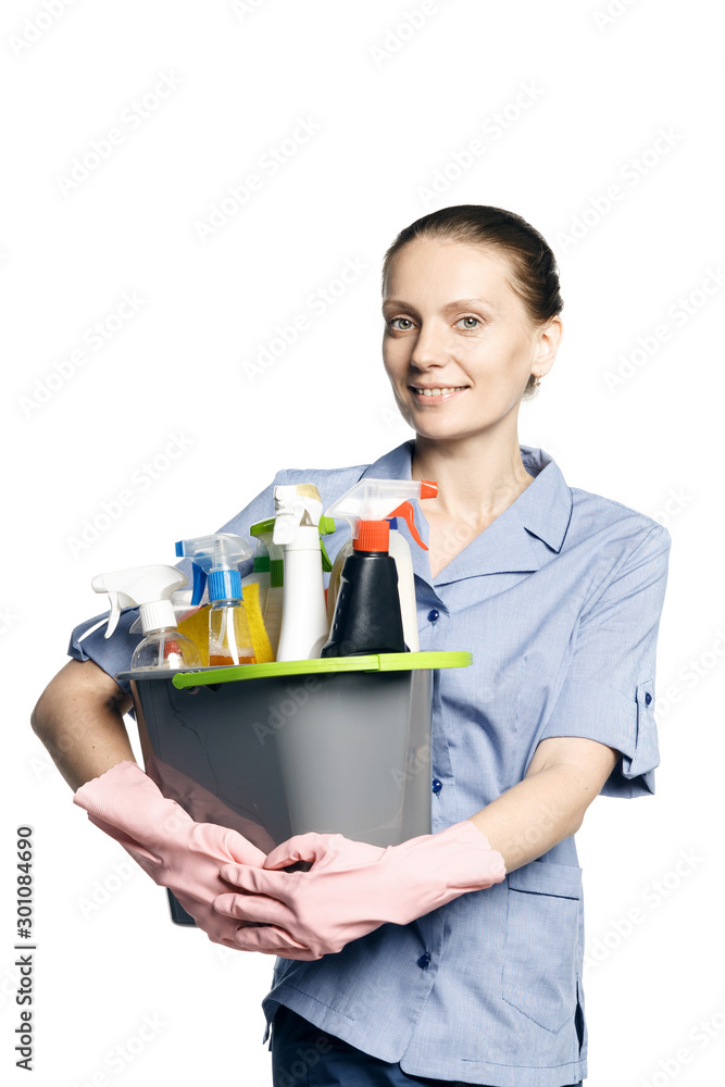 Attractive young woman in cleaning uniform and rubber gloves holding a bucket of cleaning products in her hands, isolated on white background Attractive young woman in cleaning uniform and rubber gloves holding a bucket of cleaning products in her hands, isolated on white background