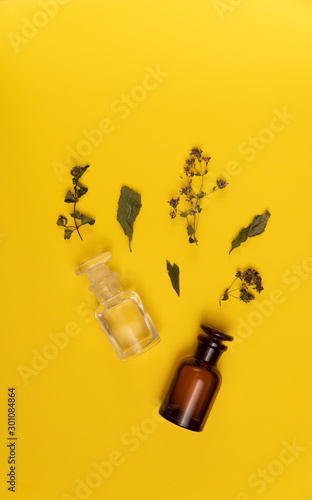 Two empty vials and dried leaves and flowers on yellow background. Perfume and medicine concept.