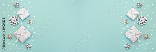 Gifts or present boxes in silver with silver bows and tree ball ornaments and little silver stars, table tob view. Composition for Christmas. Turquoise pastel background.