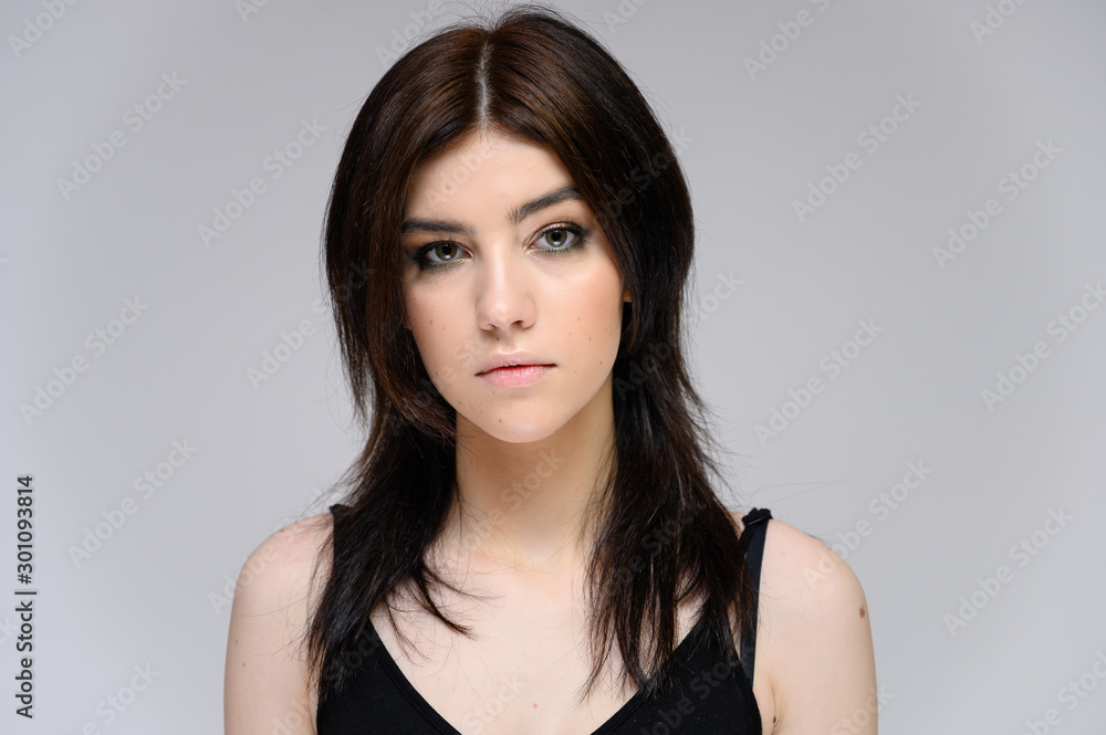 Close-up portrait of a young pretty girl with long black hair, clean skin on a gray background. The concept of cosmetics for the face, great makeup, fashionable hairstyle. Close-up portrait of a young pretty girl with long black hair, clean skin on a gray background. The concept of cosmetics for the face, great makeup, fashionable hairstyle.