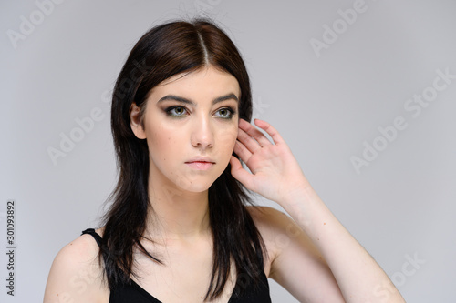 Close-up portrait of a young pretty girl with long black hair, clean skin on a gray background. The concept of cosmetics for the face, great makeup, fashionable hairstyle.