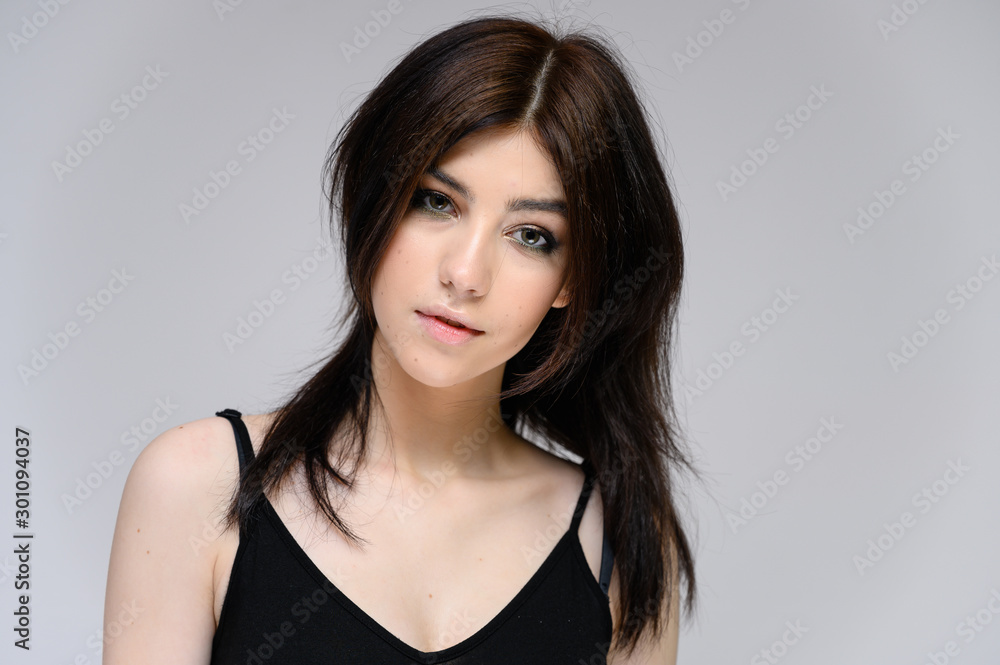 Close-up portrait of a young pretty girl with long black hair, clean skin on a gray background. The concept of cosmetics for the face, great makeup, fashionable hairstyle. Close-up portrait of a young pretty girl with long black hair, clean skin on a gray background. The concept of cosmetics for the face, great makeup, fashionable hairstyle.