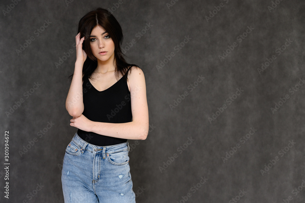 Portrait of a young pretty girl student with long black hair, on a gray background. He stands right in front of the camera, showing his hands in different poses with different emotions. Portrait of a young pretty girl student with long black hair, on a gray background. He stands right in front of the camera, showing his hands in different poses with different emotions.